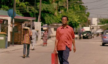 A man walking down a street holding a red suitcase