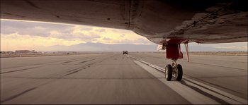 Movie still from “Face/Off” (1997), directed by John Woo – An airplane on a runway with a car in the background; Extreme Wide shot, Low angle