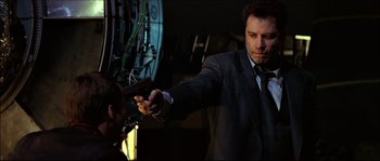 Movie still from “Face/Off” (1997), directed by John Woo – A man in a suit and tie holding a piece of food; Medium shot, Low angle