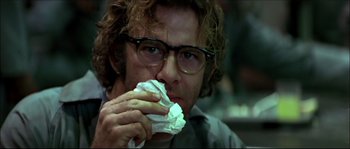 Movie still from “Face/Off” (1997), directed by John Woo – A man with glasses is eating a piece of food; Close Up shot, Low angle