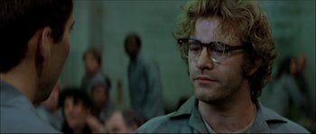 Movie still from “Face/Off” (1997), directed by John Woo – A person wearing glasses with other people in the background; Close Up shot, Over the shoulder angle