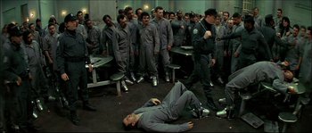 Movie still from “Face/Off” (1997), directed by John Woo – A group of men in grey suits standing around a man laying on the ground; Wide shot, High angle