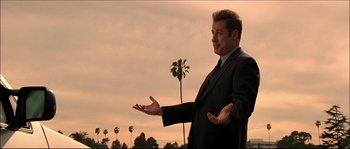 Movie still from “Face/Off” (1997), directed by John Woo – A man in a suit and tie standing in front of palm trees; Medium shot, Low angle