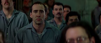 Movie still from “Face/Off” (1997), directed by John Woo – A group of people in a room looking at something; Close Up shot, Low angle