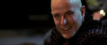 Movie still from “Face/Off” (1997), directed by John Woo – A man with a shaved head smiling for the camera; Close Up shot, Over the shoulder angle
