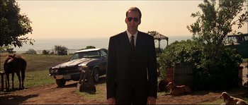 Movie still from “Face/Off” (1997), directed by John Woo – A man in a suit and tie standing in front of a car; Medium shot, Low angle