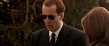 Movie still from “Face/Off” (1997), directed by John Woo – A man in a suit and sunglasses looking at the camera; Close Up shot, Over the shoulder angle