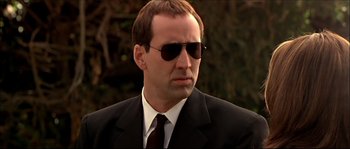 Movie still from “Face/Off” (1997), directed by John Woo – A man in a suit and sunglasses looking at the camera; Close Up shot, Low angle