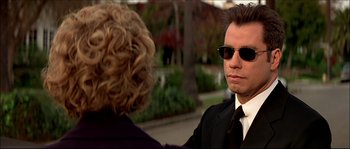 Movie still from “Face/Off” (1997), directed by John Woo – A man and a woman wearing sunglasses and a suit; Close Up shot, Over the shoulder angle