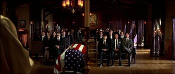 Movie still from “Face/Off” (1997), directed by John Woo – A group of people sitting in front of an american flag draped casket; Wide shot, High angle