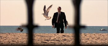 Movie still from “Face/Off” (1997), directed by John Woo – A man standing on the beach looking at a bird; Wide shot, Low angle