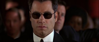 Movie still from “Face/Off” (1997), directed by John Woo – A person wearing a suit and sunglasses; Close Up shot, Low angle