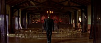 Movie still from “Face/Off” (1997), directed by John Woo – A man in a black suit walking in front of a stage; Wide shot, Low angle