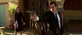 Movie still from “Face/Off” (1997), directed by John Woo – A man in a suit and tie holding a gun in his hand; Medium shot, Low angle