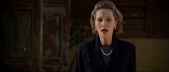 Movie still from “Face/Off” (1997), directed by John Woo – An older woman wearing a black jacket and a pearl necklace; Close Up shot, Over the shoulder angle