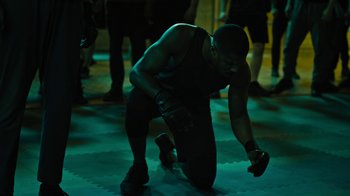 Movie still from “Fahrenheit 451” (2018), directed by Ramin Bahrani – A man in a black shirt is squatting on the ground; Medium shot, High angle