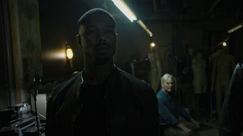 Movie still from “Fahrenheit 451” (2018), directed by Ramin Bahrani – A man standing in a dark room next to another man; Medium shot, Over the shoulder angle