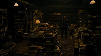 Movie still from “Fahrenheit 451” (2018), directed by Ramin Bahrani – A man standing next to a large pile of books; Wide shot, High angle