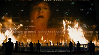 Movie still from “Fahrenheit 451” (2018), directed by Ramin Bahrani – People standing in front of a large screen with a woman's face on it; Extreme Wide shot, Low angle