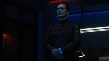 Movie still from “Fahrenheit 451” (2018), directed by Ramin Bahrani – A man standing in a dark room with his arms crossed; Medium shot, Low angle
