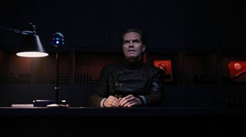 Movie still from “Fahrenheit 451” (2018), directed by Ramin Bahrani – A man sitting at a table in a dark room; Medium shot, Low angle