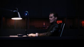 Movie still from “Fahrenheit 451” (2018), directed by Ramin Bahrani – A man sitting at a desk in a dark room; Medium shot, High angle