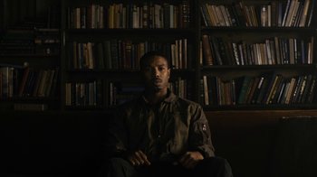 Movie still from “Fahrenheit 451” (2018), directed by Ramin Bahrani – A man sitting in front of a book shelf; Medium shot, High angle