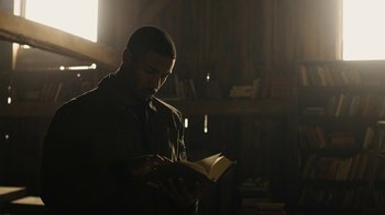 Movie still from “Fahrenheit 451” (2018), directed by Ramin Bahrani – A man is reading a book in the dark; Medium shot, High angle