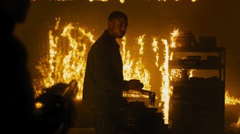 Movie still from “Fahrenheit 451” (2018), directed by Ramin Bahrani – A man standing in front of a fire holding a cage; Medium shot, Over the shoulder angle