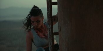 Movie still from “Fall” (2022), directed by Scott Mann – A woman in a grey tank top with a knife in her mouth; Close Up shot, High angle