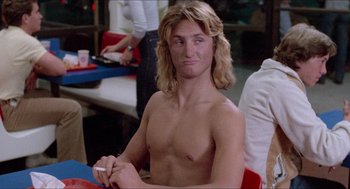 Movie still from “Fast Times at Ridgemont High” (1982), directed by Amy Heckerling – A shirtless man sitting in front of a table; Medium shot, Over the shoulder angle