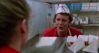 Movie still from “Fast Times at Ridgemont High” (1982), directed by Amy Heckerling – A person wearing a hat sitting in front of a counter; Close Up shot, Over the shoulder angle