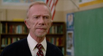 Movie still from “Fast Times at Ridgemont High” (1982), directed by Amy Heckerling – An older man wearing a suit and tie in front of a book shelf; Close Up shot, Low angle