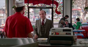 Movie still from “Fast Times at Ridgemont High” (1982), directed by Amy Heckerling – A man in a suit and tie standing at a counter; Medium shot, Over the shoulder angle