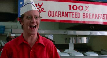 Movie still from “Fast Times at Ridgemont High” (1982), directed by Amy Heckerling – A man wearing a paper chef's hat standing in front of a sign; Close Up shot, Low angle