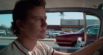 Movie still from “Fast Times at Ridgemont High” (1982), directed by Amy Heckerling – A man sitting in the driver's seat of a car driving down a street; Close Up shot, Low angle