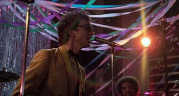 Movie still from “Fast Times at Ridgemont High” (1982), directed by Amy Heckerling – A man with a microphone in front of a group of people; Medium shot, Low angle