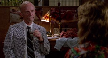 Movie still from “Fast Times at Ridgemont High” (1982), directed by Amy Heckerling – An older man in a plaid jacket holding a tie; Medium shot, Over the shoulder angle