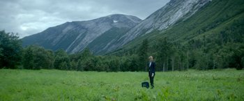 Movie still from “Ex Machina” (2014), directed by Alex Garland – A man standing in a grassy field with a suitcase; Extreme Wide shot, High angle
