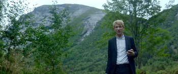Movie still from “Ex Machina” (2014), directed by Alex Garland – A man in a suit standing in front of a mountain; Medium shot, Low angle