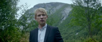 Movie still from “Ex Machina” (2014), directed by Alex Garland – A man standing in front of a mountain with trees in the background; Close Up shot, Over the shoulder angle