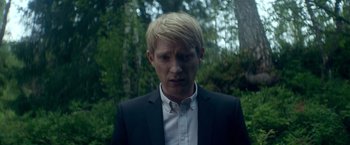 Movie still from “Ex Machina” (2014), directed by Alex Garland – A man with blonde hair wearing a black suit and striped shirt; Close Up shot, Low angle