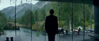Movie still from “Ex Machina” (2014), directed by Alex Garland – A man standing in front of a window looking out at the mountains; Wide shot, Over the shoulder angle