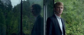 Movie still from “Ex Machina” (2014), directed by Alex Garland – A man standing in front of a window with trees in the background; Medium shot, Over the shoulder angle