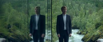 Movie still from “Ex Machina” (2014), directed by Alex Garland – A man standing in front of a mirror in front of a forest; Medium shot, Over the shoulder angle