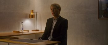 Movie still from “Ex Machina” (2014), directed by Alex Garland – A man sitting at a table wearing a suit and tie; Medium shot, High angle