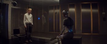 Movie still from “Ex Machina” (2014), directed by Alex Garland – A woman sitting on a bench next to a man in front of a mirror; Wide shot, Over the shoulder angle