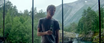 Movie still from “Ex Machina” (2014), directed by Alex Garland – A young man holding a bottle of beer in front of a window; Medium shot, Over the shoulder angle