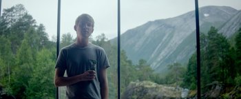 Movie still from “Ex Machina” (2014), directed by Alex Garland – A man standing in front of a window with a mountain view; Medium shot, Low angle