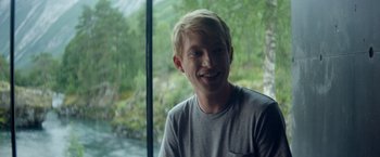 Movie still from “Ex Machina” (2014), directed by Alex Garland – A young man smiling in front of a window; Close Up shot, Over the shoulder angle